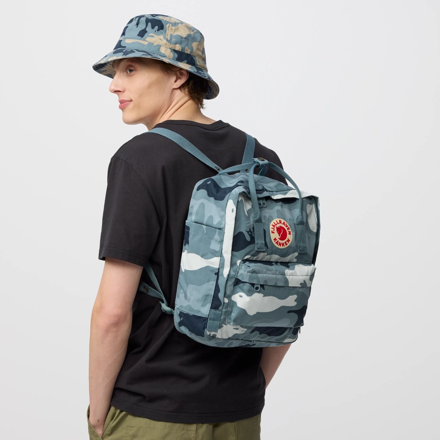 Person wearing a camouflage backpack and hat on a white background