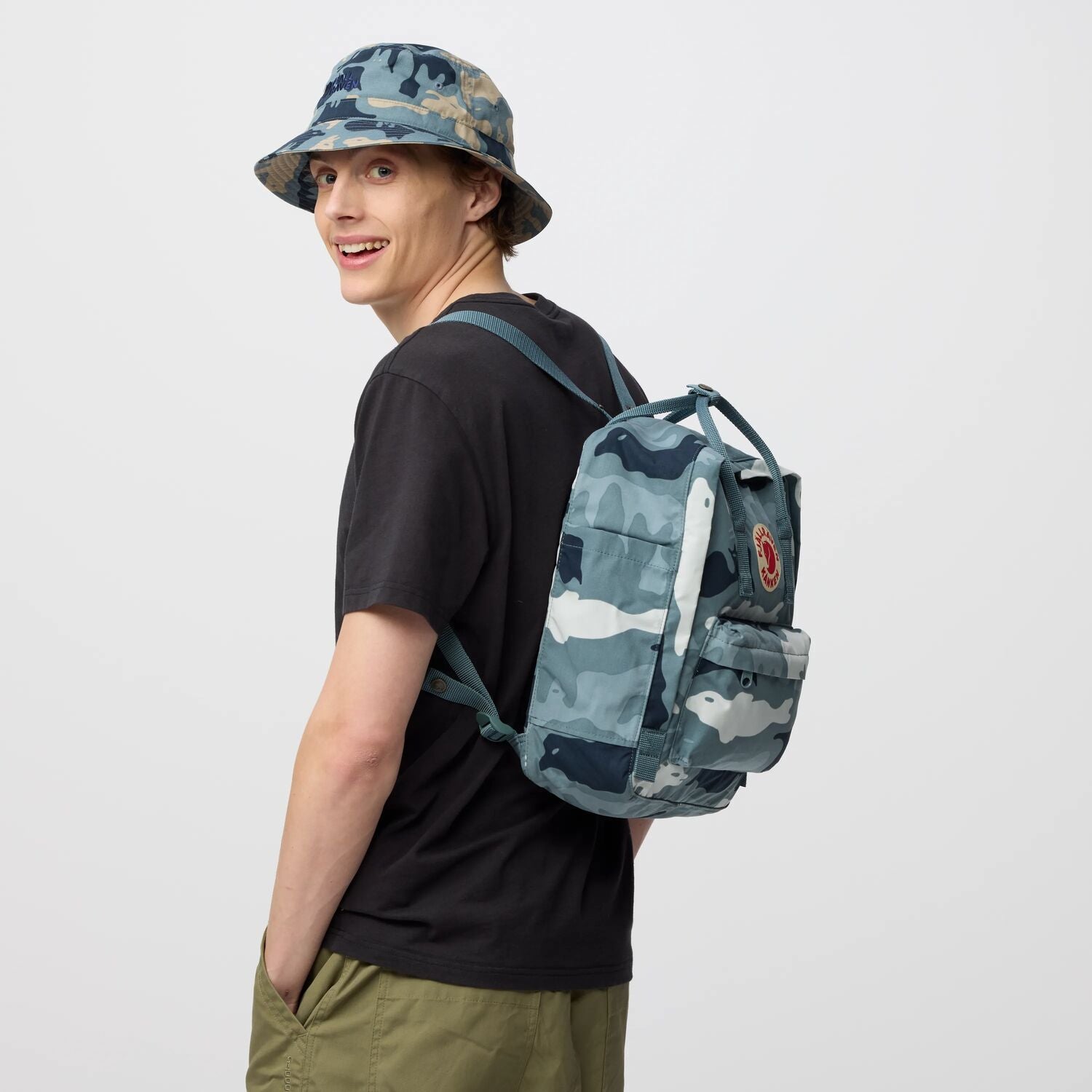 Person wearing a camouflage backpack and hat on a plain background