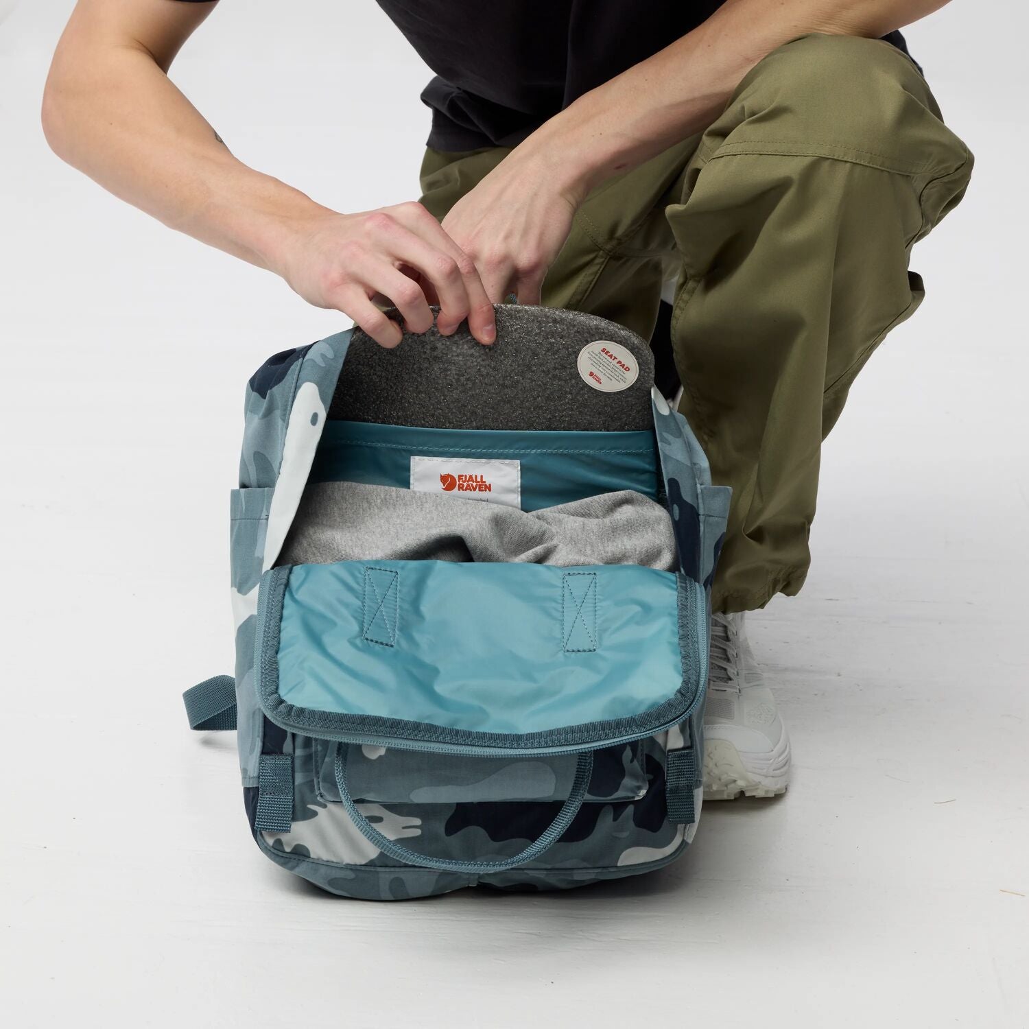 Person opening a blue camouflage backpack on a white background
