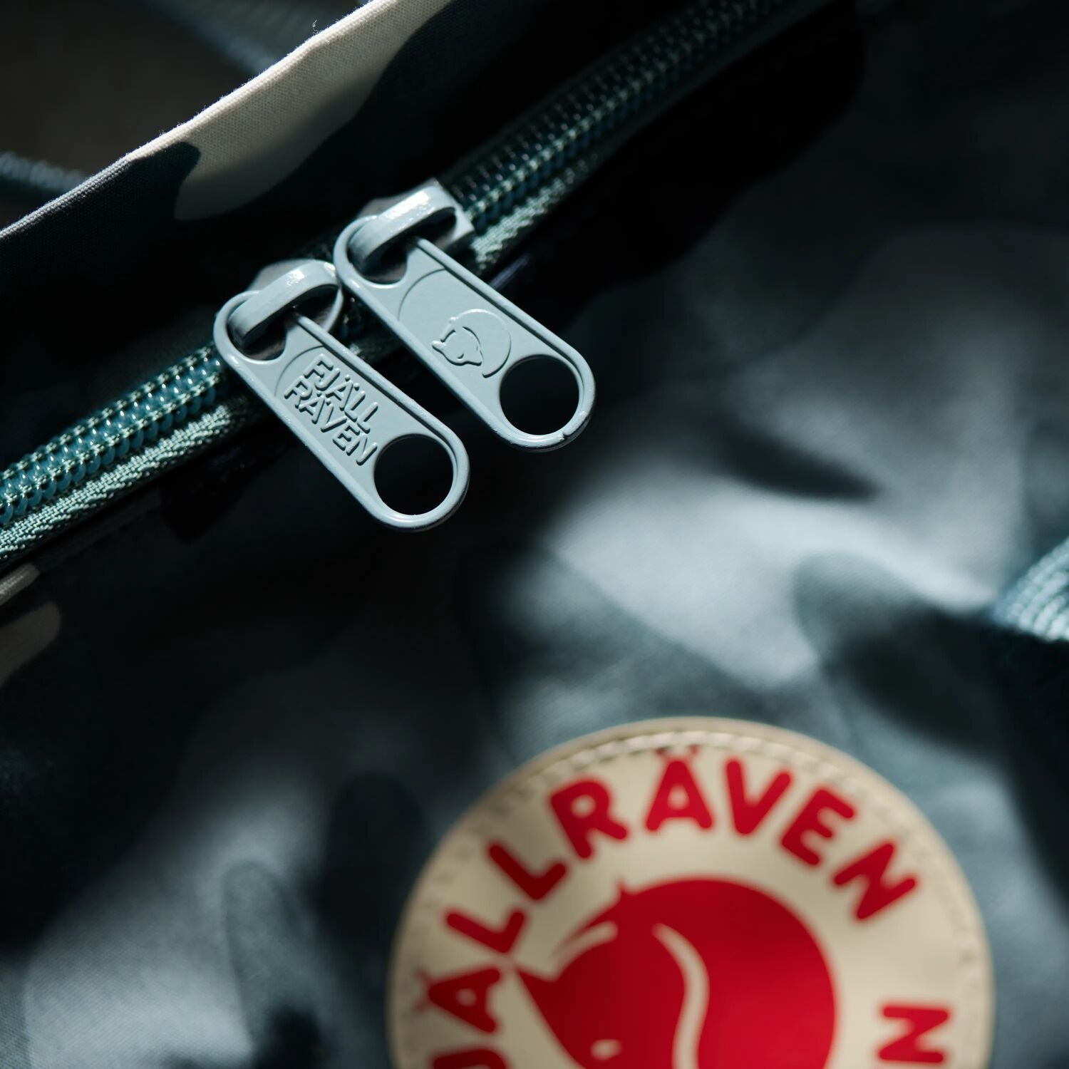 Close-up of a Fjällräven patch on a textured surface with zippers.