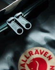 Close-up of a Fjällräven patch on a textured surface with zippers.