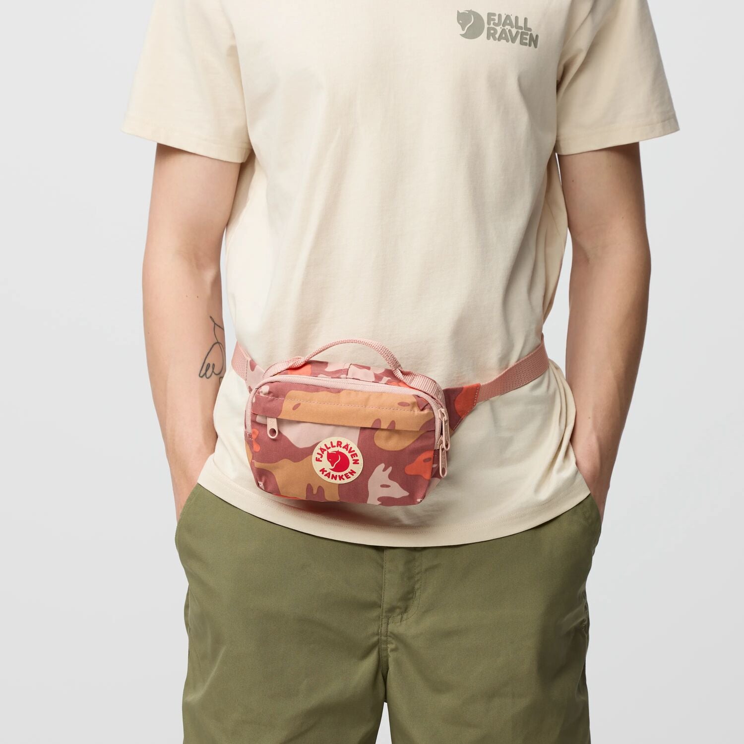 Person wearing a beige t-shirt and green pants with a red and brown patterned waist bag.