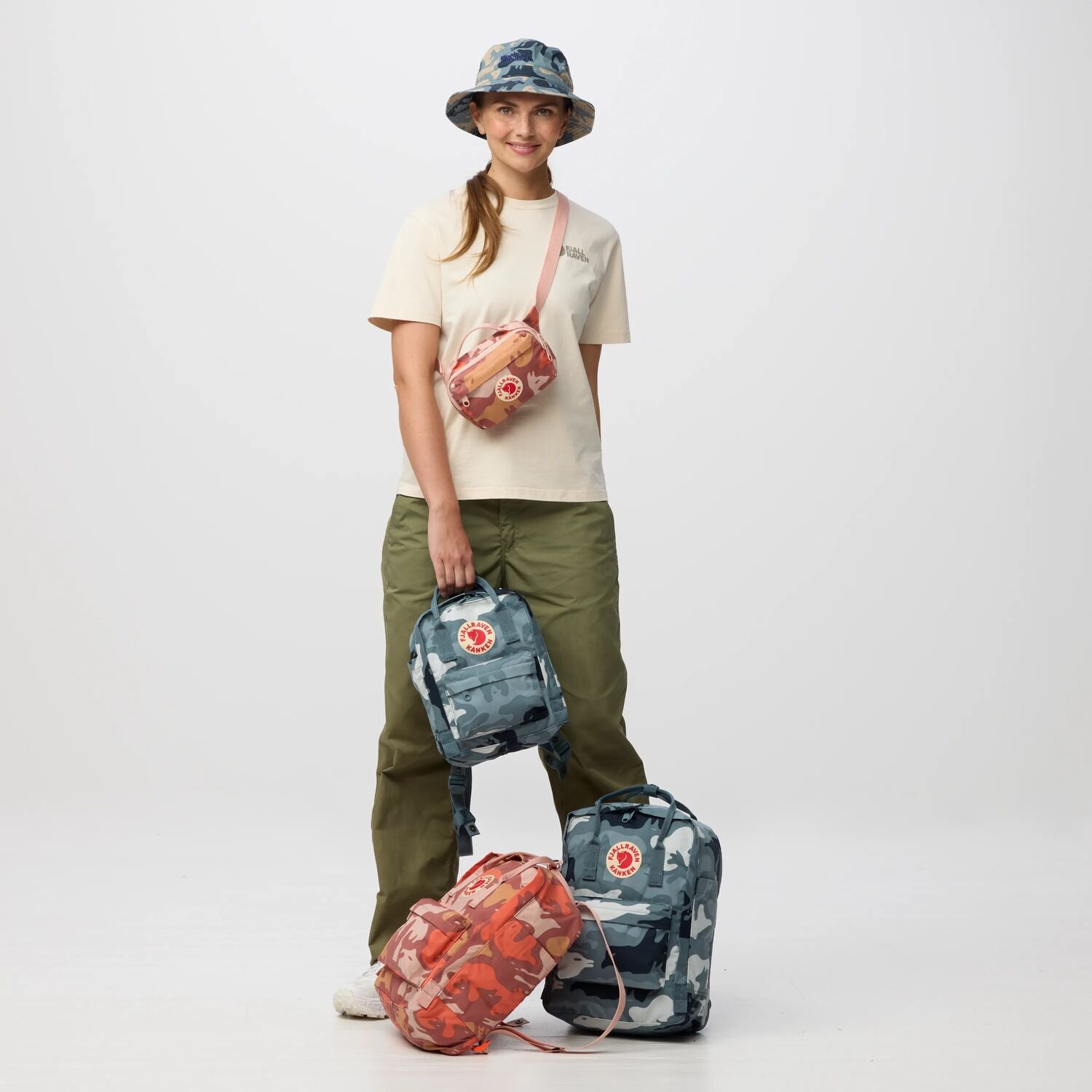 Person holding a camouflage backpack with two additional bags on a white background