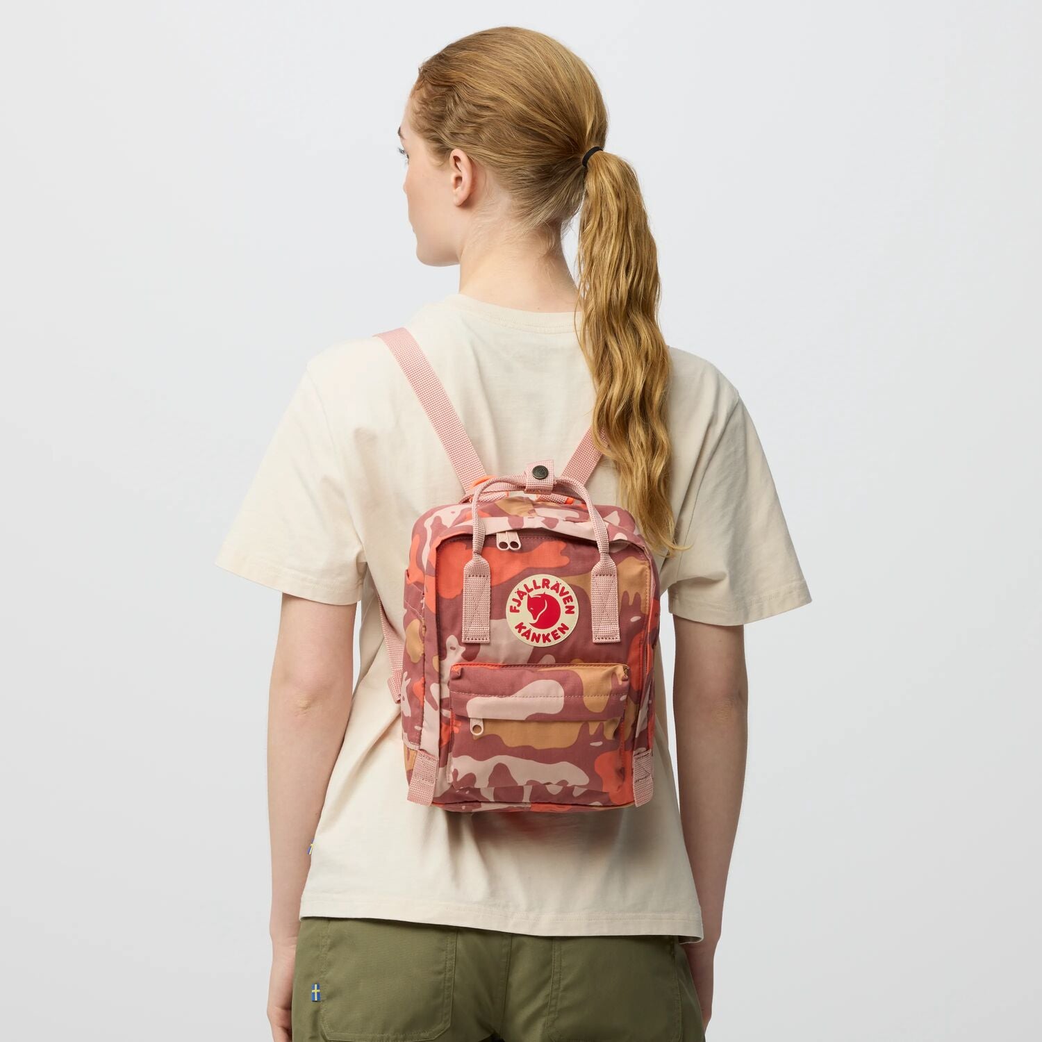 Person wearing a red and orange camouflage backpack with a visible brand logo on a light gray background