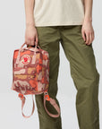 Person holding a camouflage-patterned backpack with a neutral background