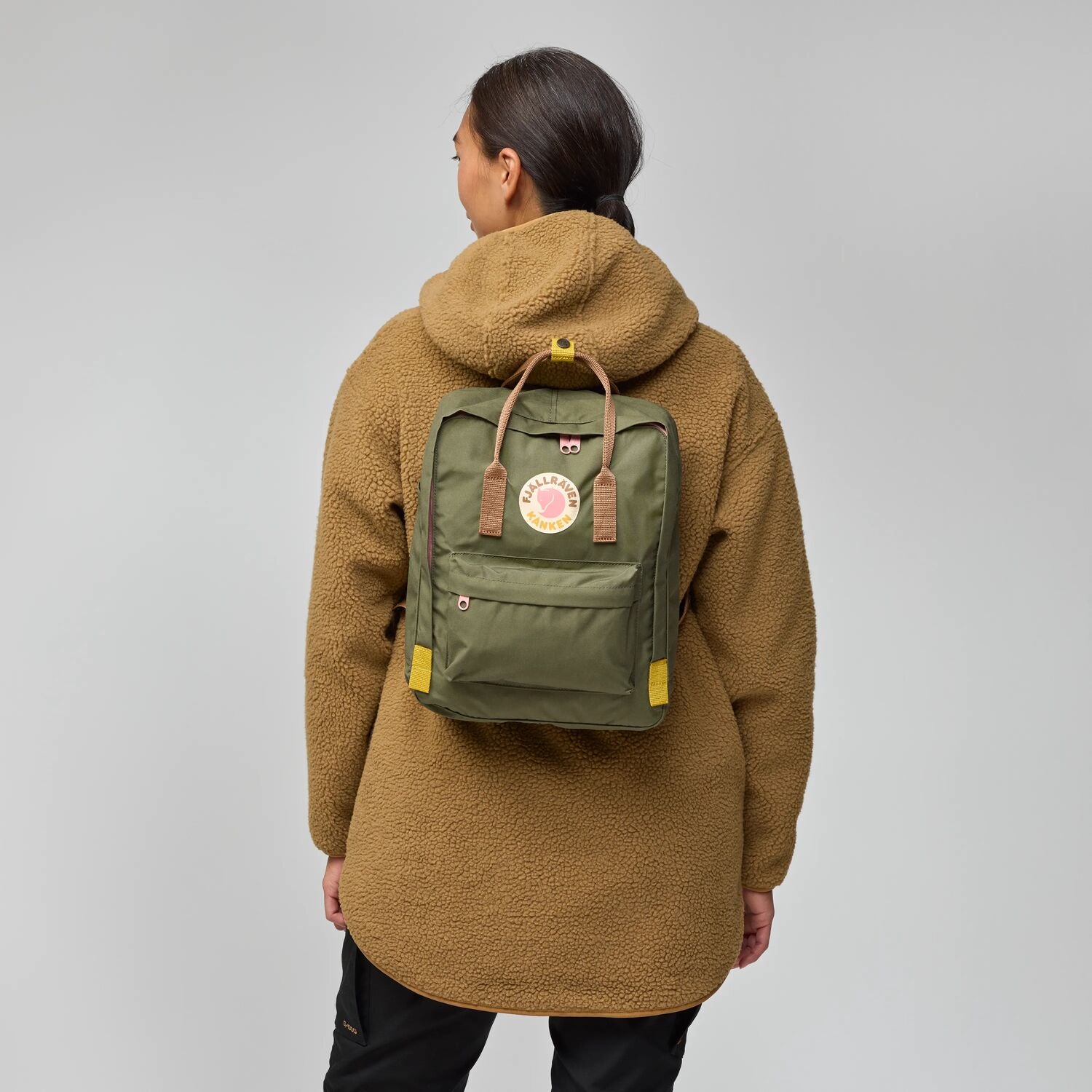 Person wearing a brown fleece jacket with a green backpack on a gray background