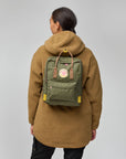 Person wearing a brown fleece jacket with a green backpack on a gray background