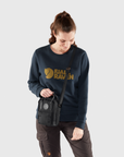 Woman wearing a navy Fjällräven sweatshirt holding a black bag on a light gray background