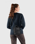 Person wearing a dark blue sweatshirt with a black crossbody bag on a light gray background