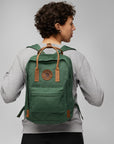 Person wearing a green backpack with a visible Fjällräven logo on a gray background