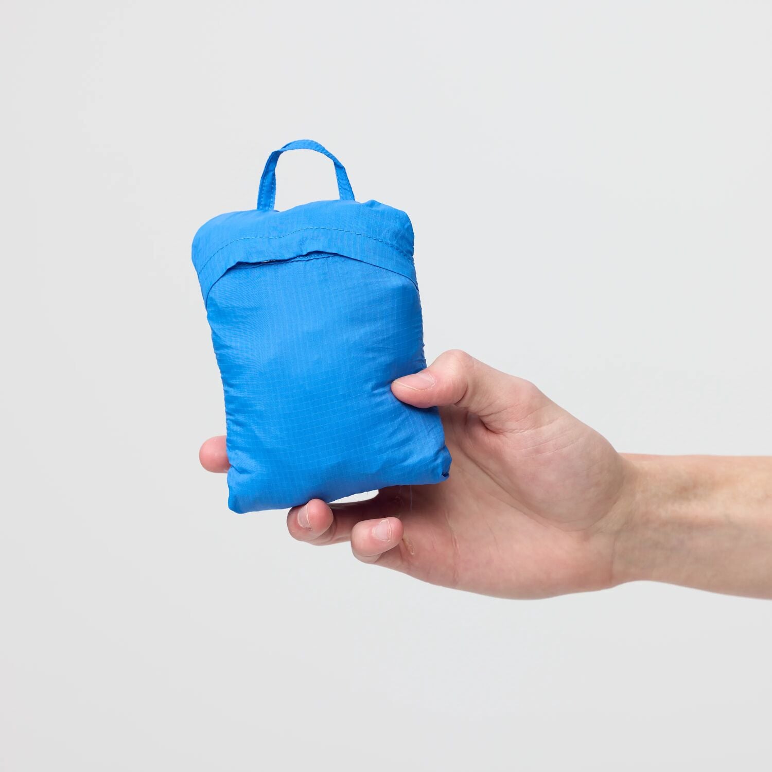Hand holding a small blue pack against a light gray background