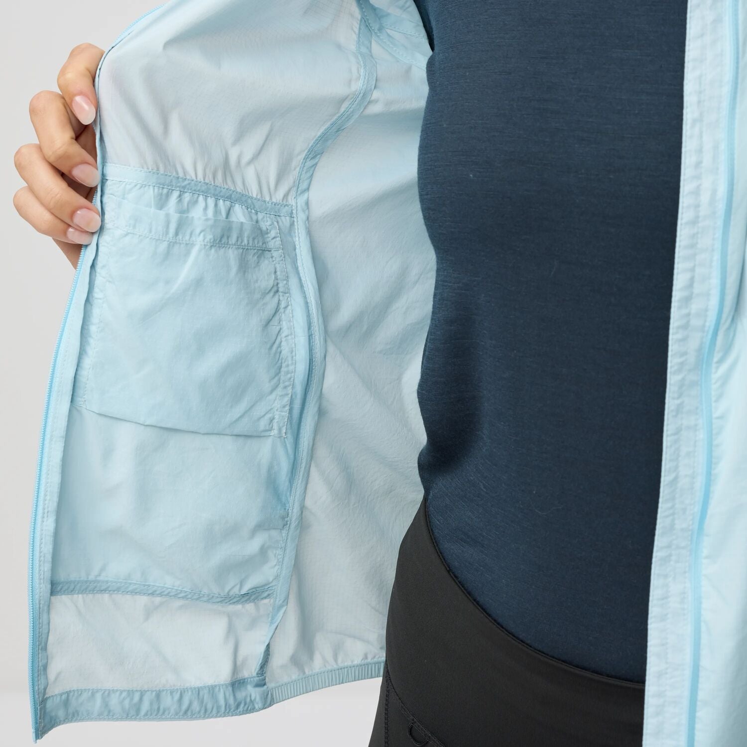 Light blue jacket with a pocket held open by a hand on a light gray background