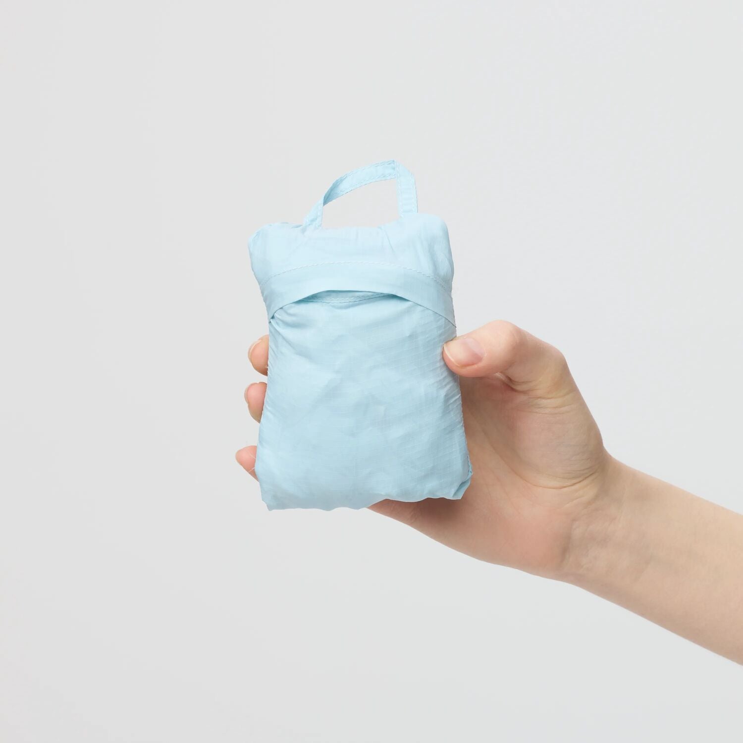 Hand holding a light blue packable jacket against a plain background