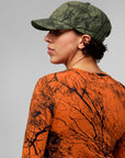 Person wearing a camouflage cap and shirt with a tree branch pattern on a gray background