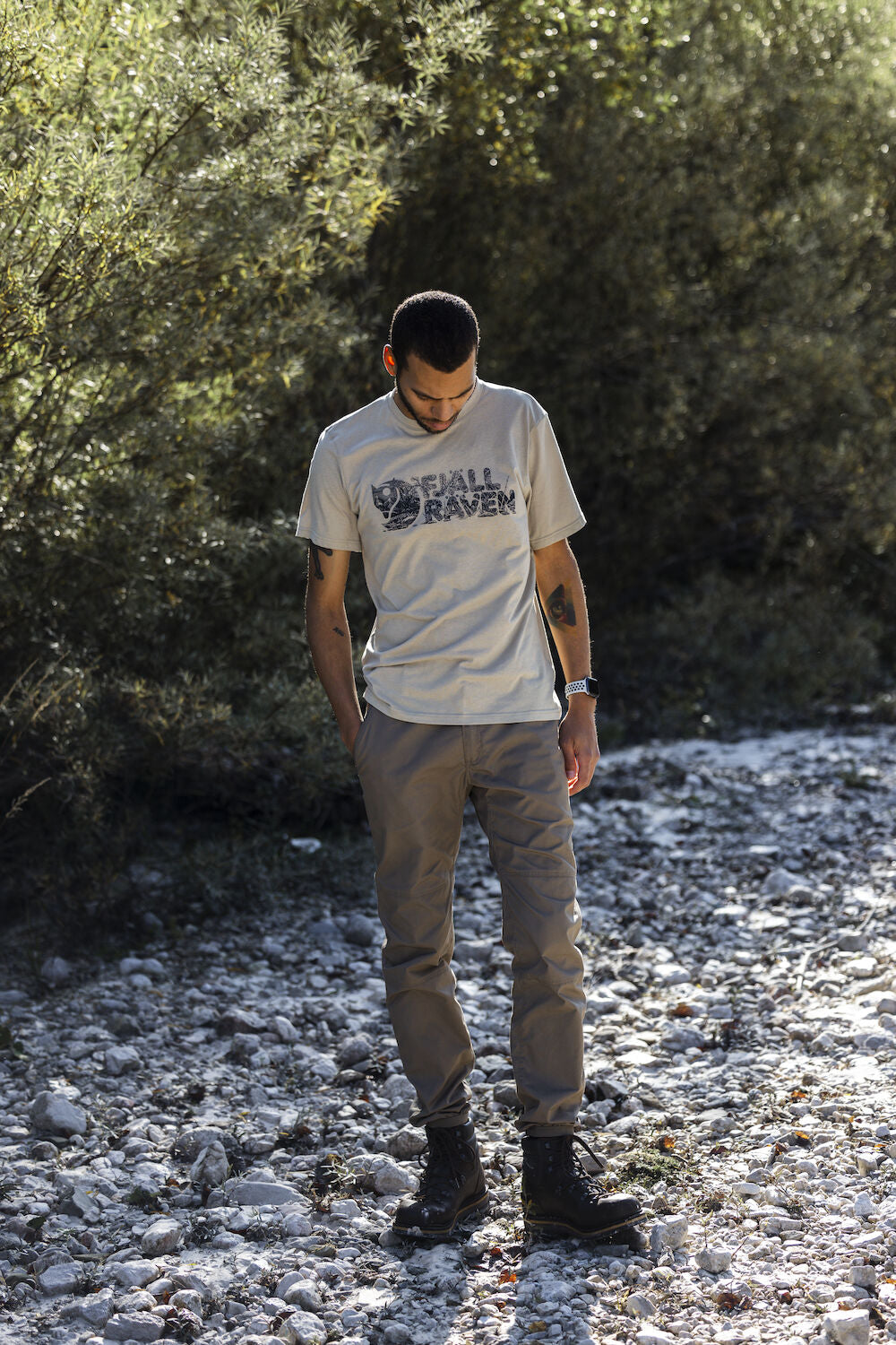 man wearing a fossilround neck t-shirt  standing on pebbled stones