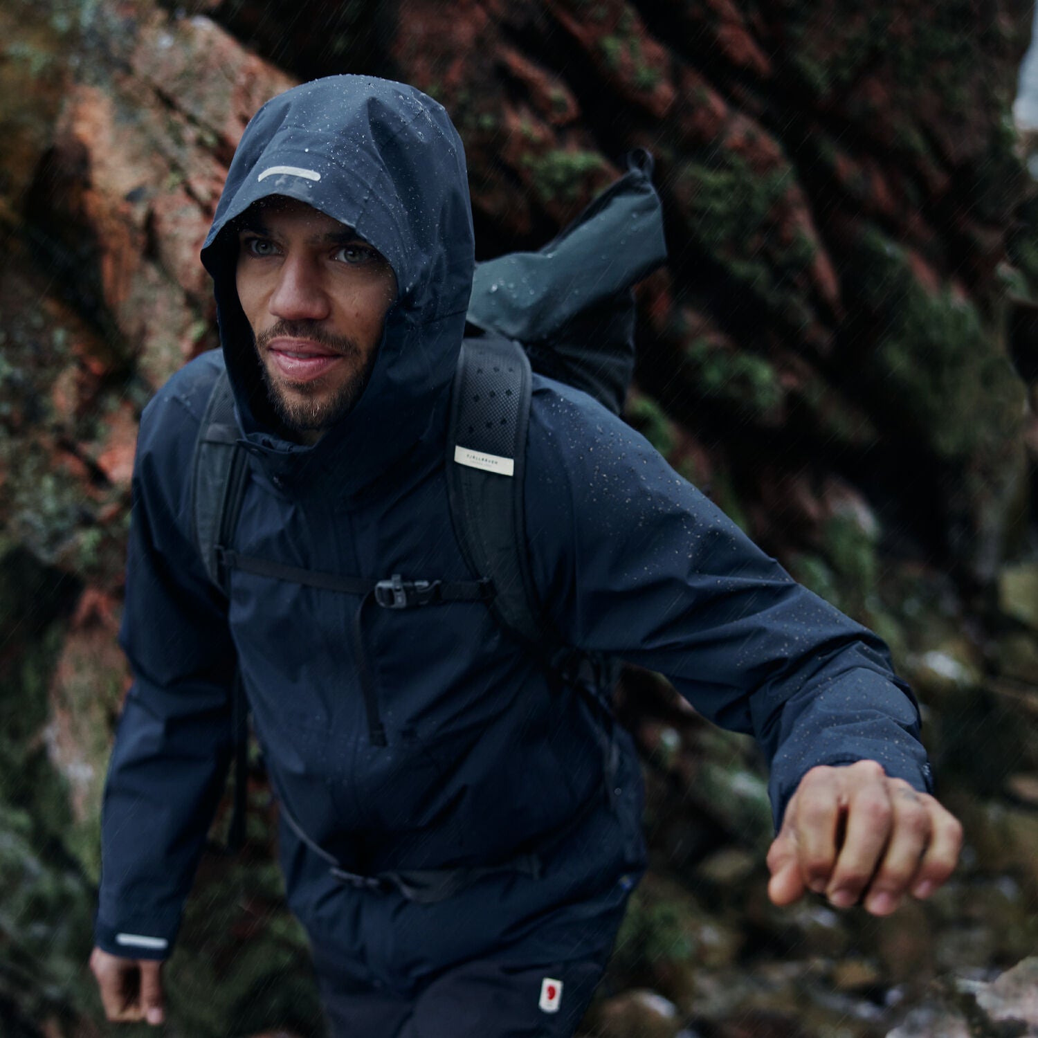 man in navy windbreaker jacket with hood trekking in mountain