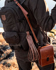 Person wearing a dark jacket and carrying a brown leather bag with a scenic background