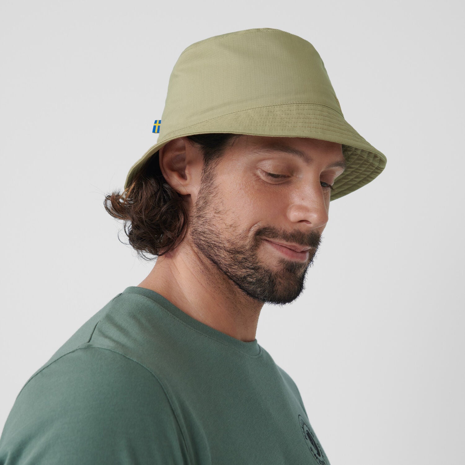 Man wearing a green bucket hat with a small flag emblem on a plain background