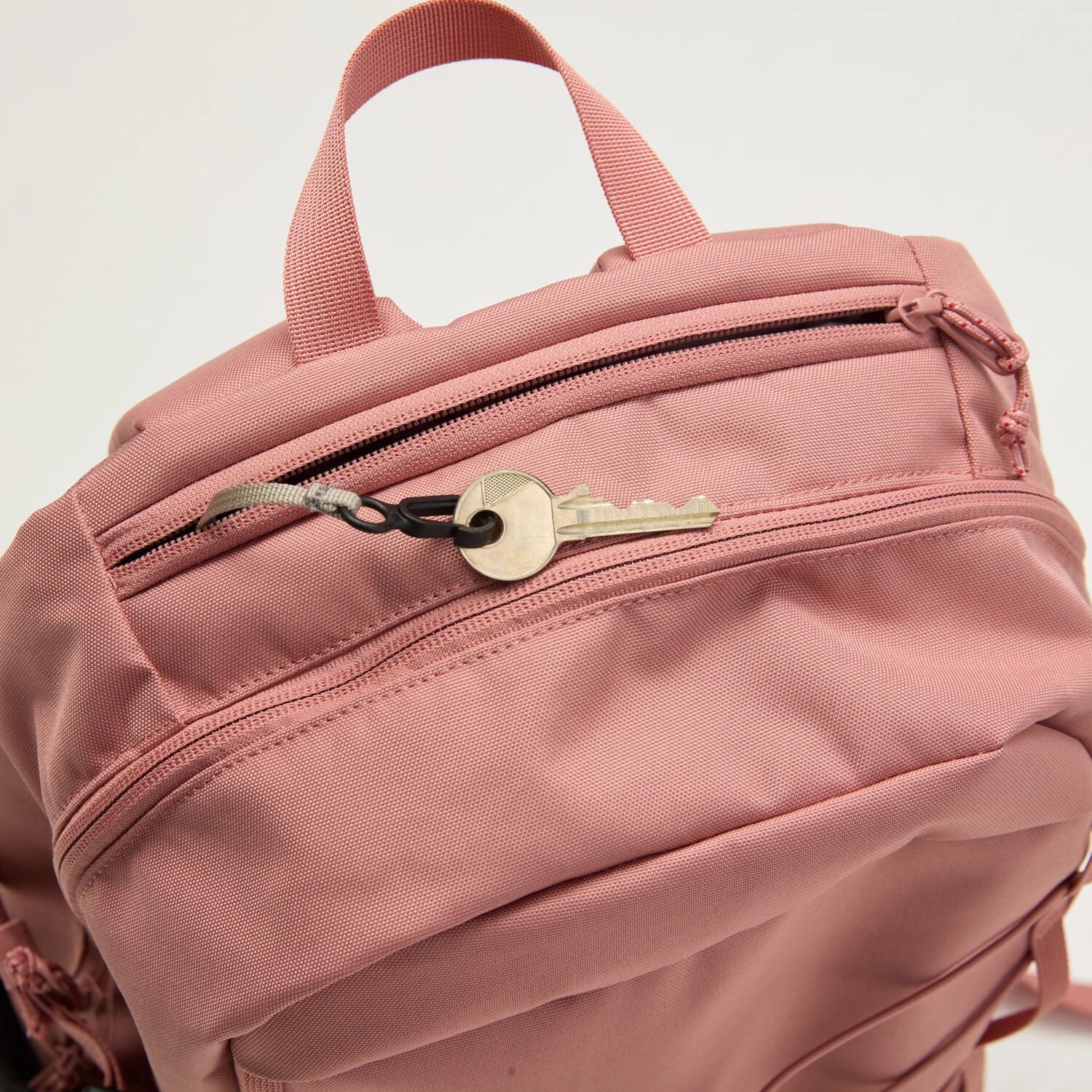 Pink backpack with a key attached to one of its zippers on a light gray background
