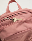 Pink backpack with a key attached to one of its zippers on a light gray background