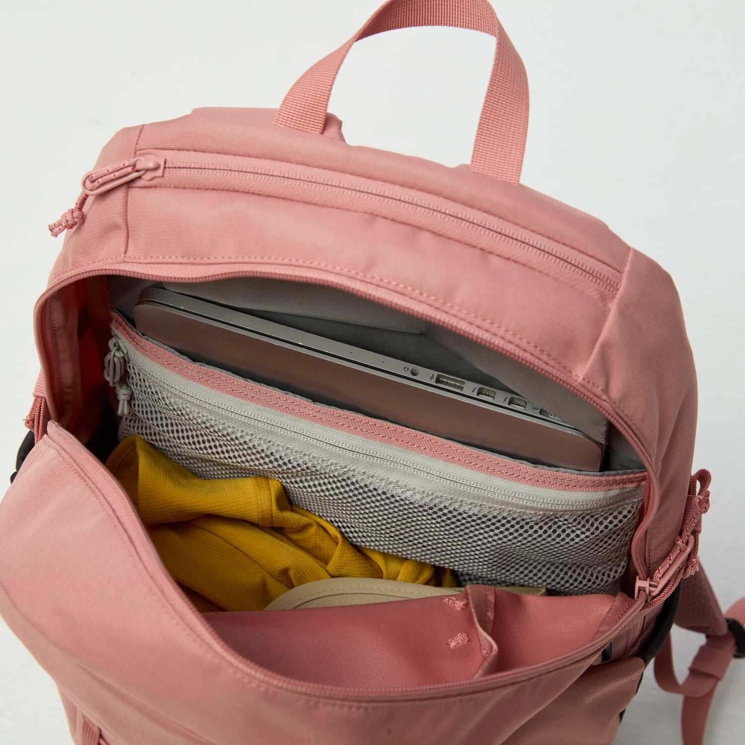 Pink backpack with compartments containing a laptop, yellow item, and gray item on a white background
