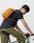 Person riding a bicycle with a yellow backpack on a plain background