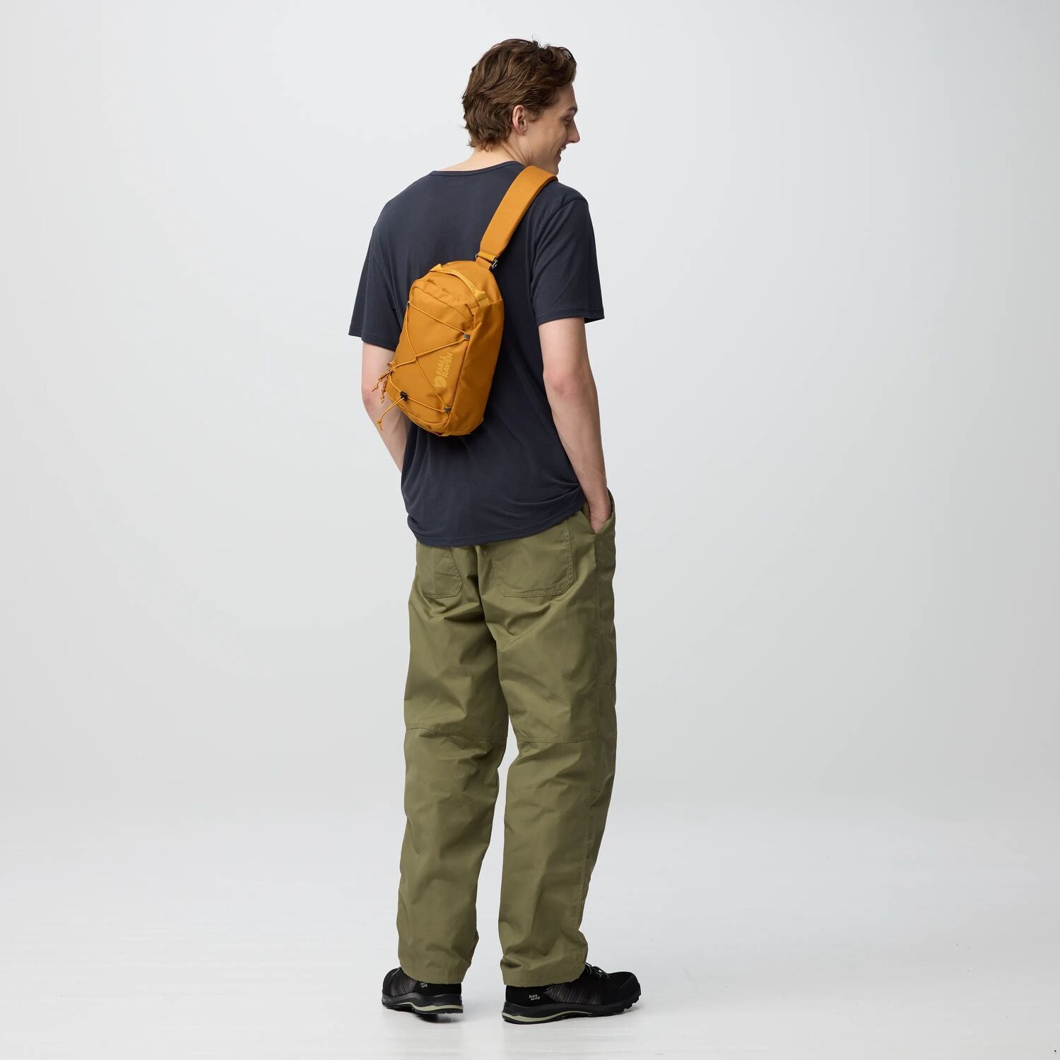 Person wearing a dark blue shirt, green pants, and an orange backpack on a white background