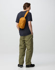 Person wearing a dark blue shirt, green pants, and an orange backpack on a white background