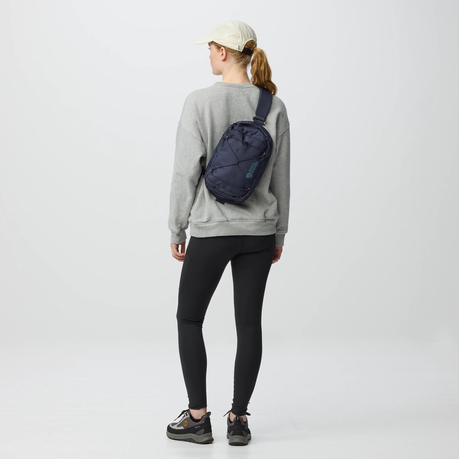Person wearing a gray sweatshirt and black leggings with a navy crossbody bag on a white background