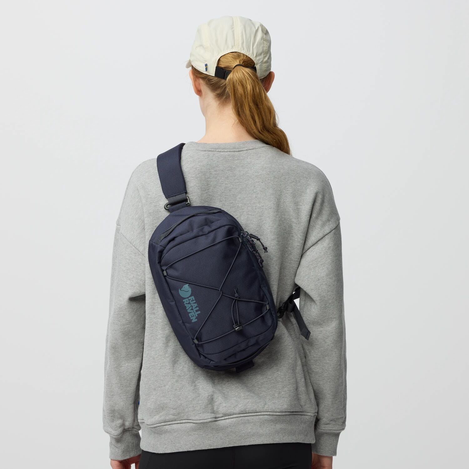 Person wearing a gray sweatshirt with a navy sling bag on a light gray background