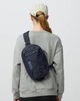 Person wearing a gray sweatshirt with a navy sling bag on a light gray background