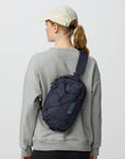 Person wearing a gray sweatshirt with a navy sling bag on a white background