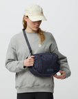 Person wearing a gray sweatshirt and beige cap holding a navy blue bag against a light gray background