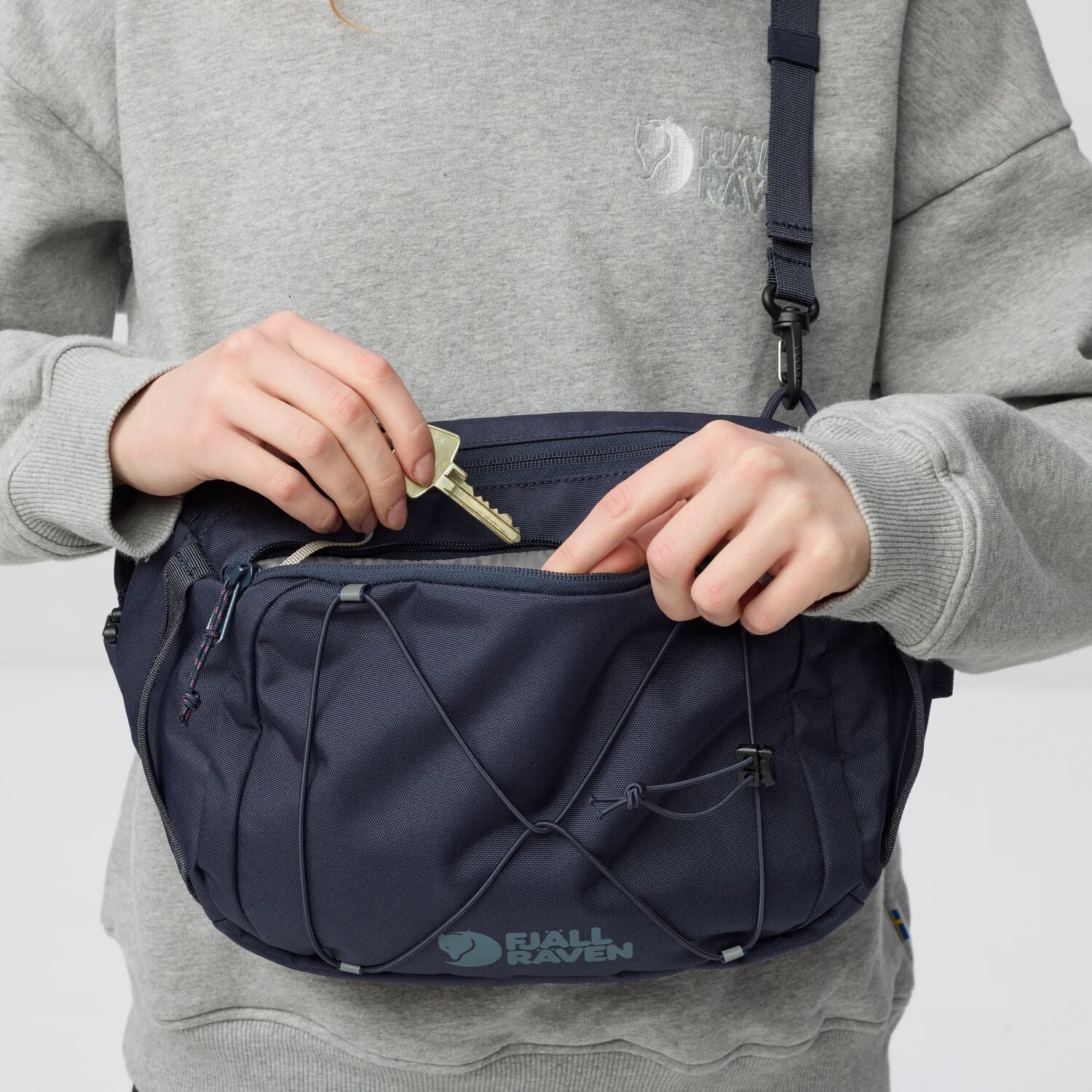 Person opening a navy blue Fjällräven bag with a key against a light gray background