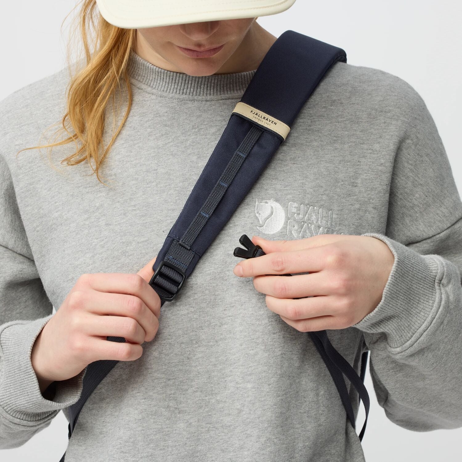 Person adjusting a navy backpack strap on a plain background