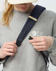 Person adjusting a navy backpack strap on a plain background