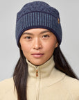 Woman wearing a blue knit beanie and beige jacket on a gray background