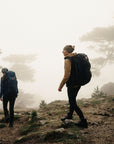 Two hikers with backpacks walking on a misty forest trail.