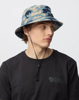 Person wearing a camouflage bucket hat and black t-shirt with a Fjällräven logo on a light gray background