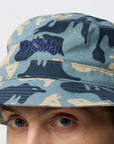 Person wearing a camouflage bucket hat with Fjällräven logo on a white background