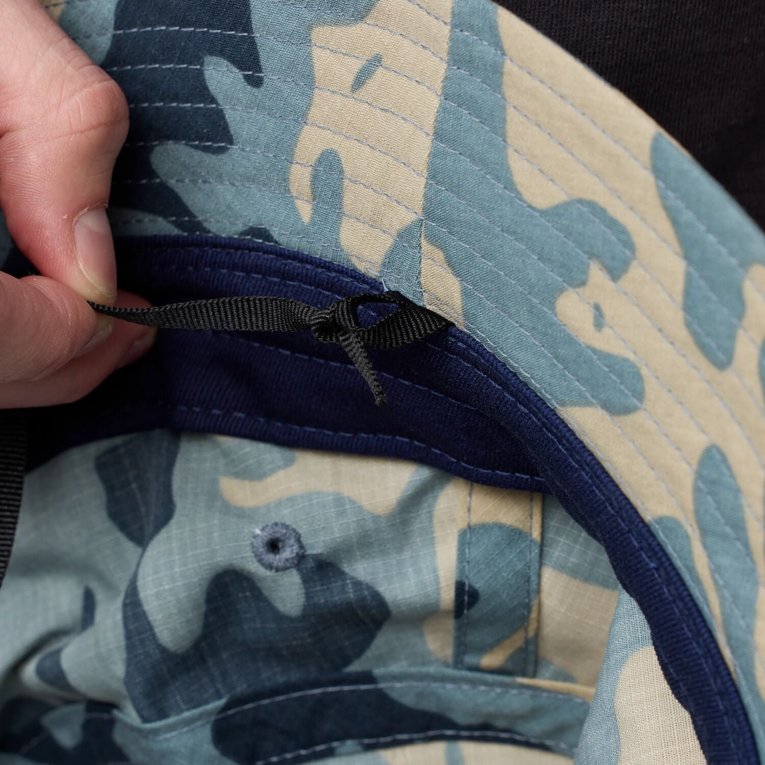 Close-up of a camouflage-patterned fabric with a hand adjusting a black strap.