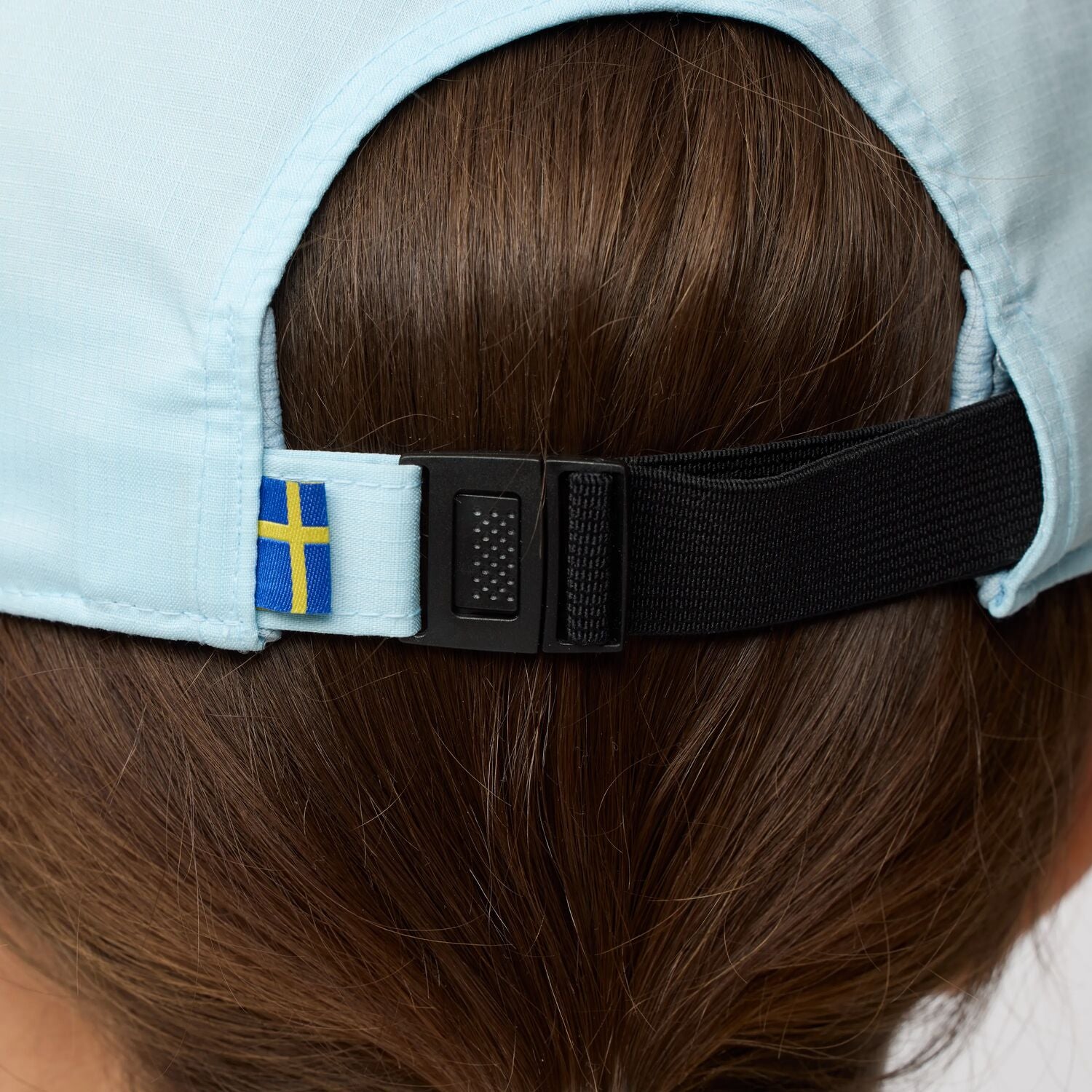 Close-up of a cap with a Swedish flag on the strap, worn by a person.