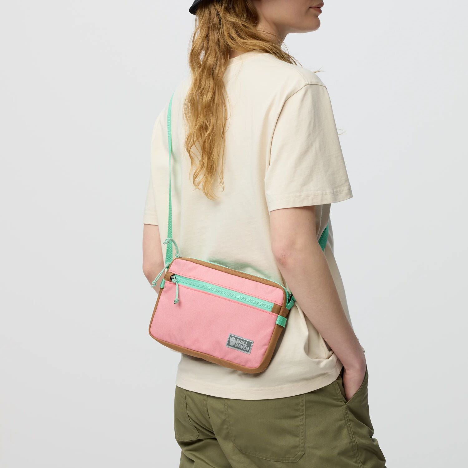 Person wearing a pink crossbody bag with green accents on a plain background
