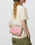 Person wearing a pink crossbody bag with green accents on a plain background