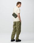Person wearing a beige shirt and green pants with a green bag on a white background