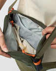 Person opening a green bag with orange zippers on a light gray background
