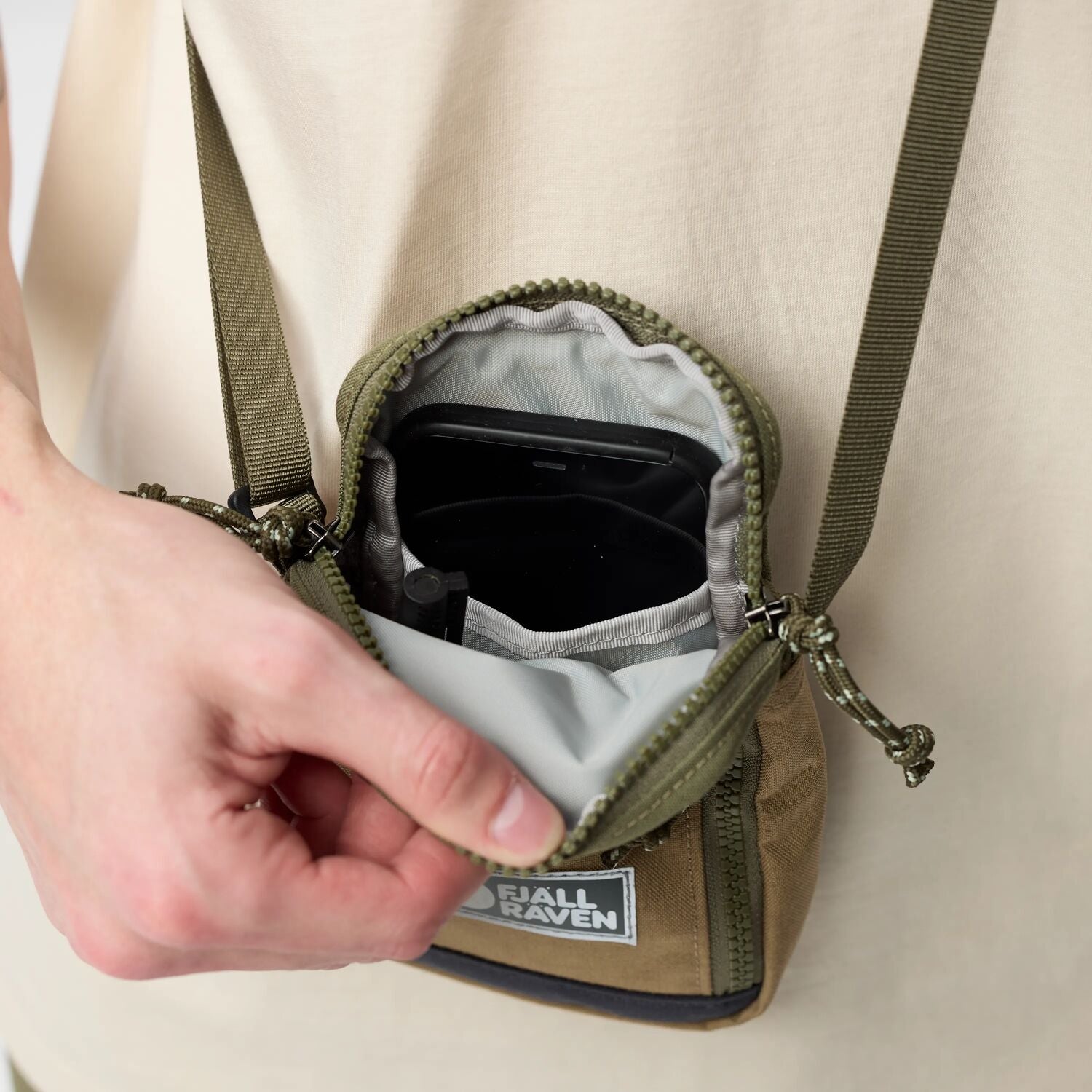 Person opening a small green bag with a visible fjallraven label on a beige background