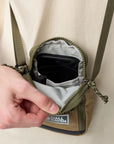 Person opening a small green bag with a visible fjallraven label on a beige background