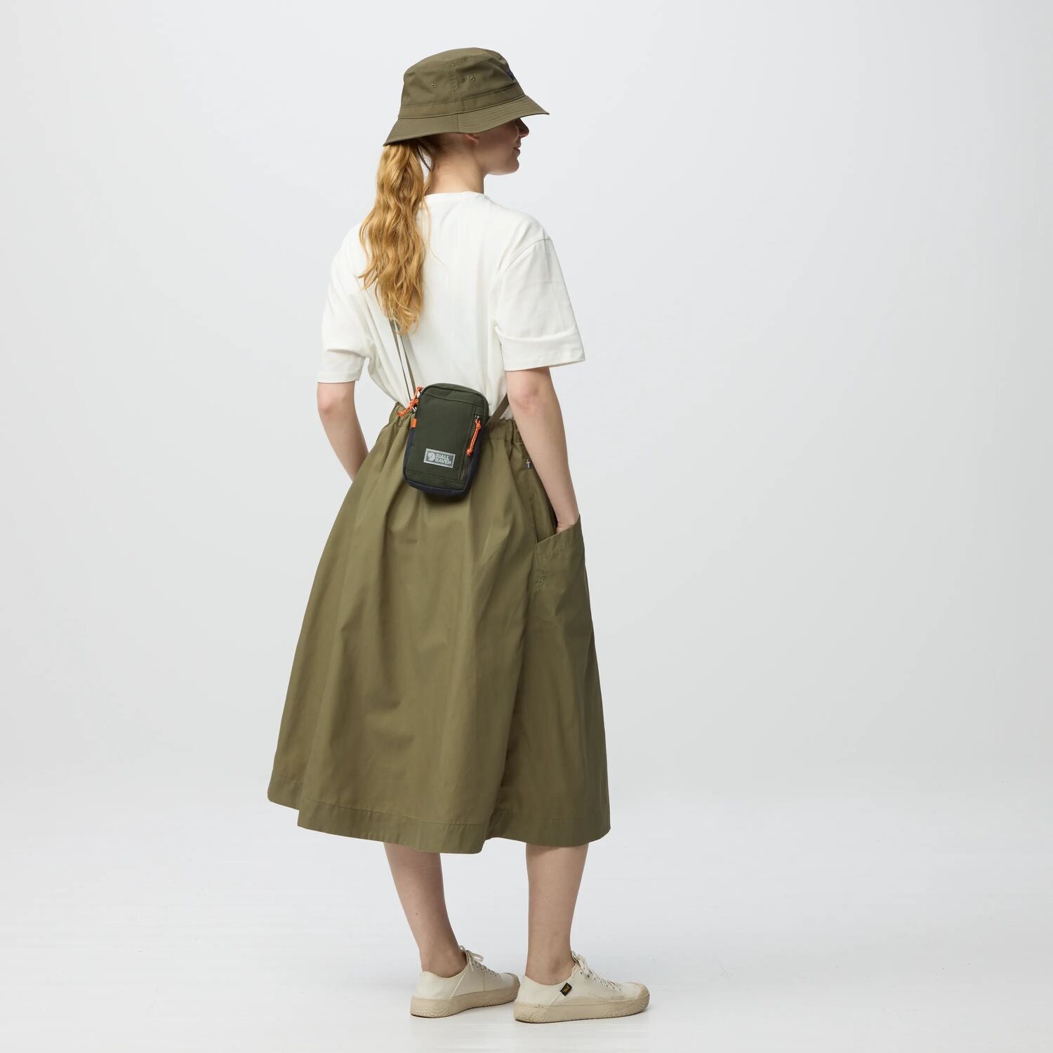 Person wearing a green skirt, white shirt, and hat, holding a black bag on a white background