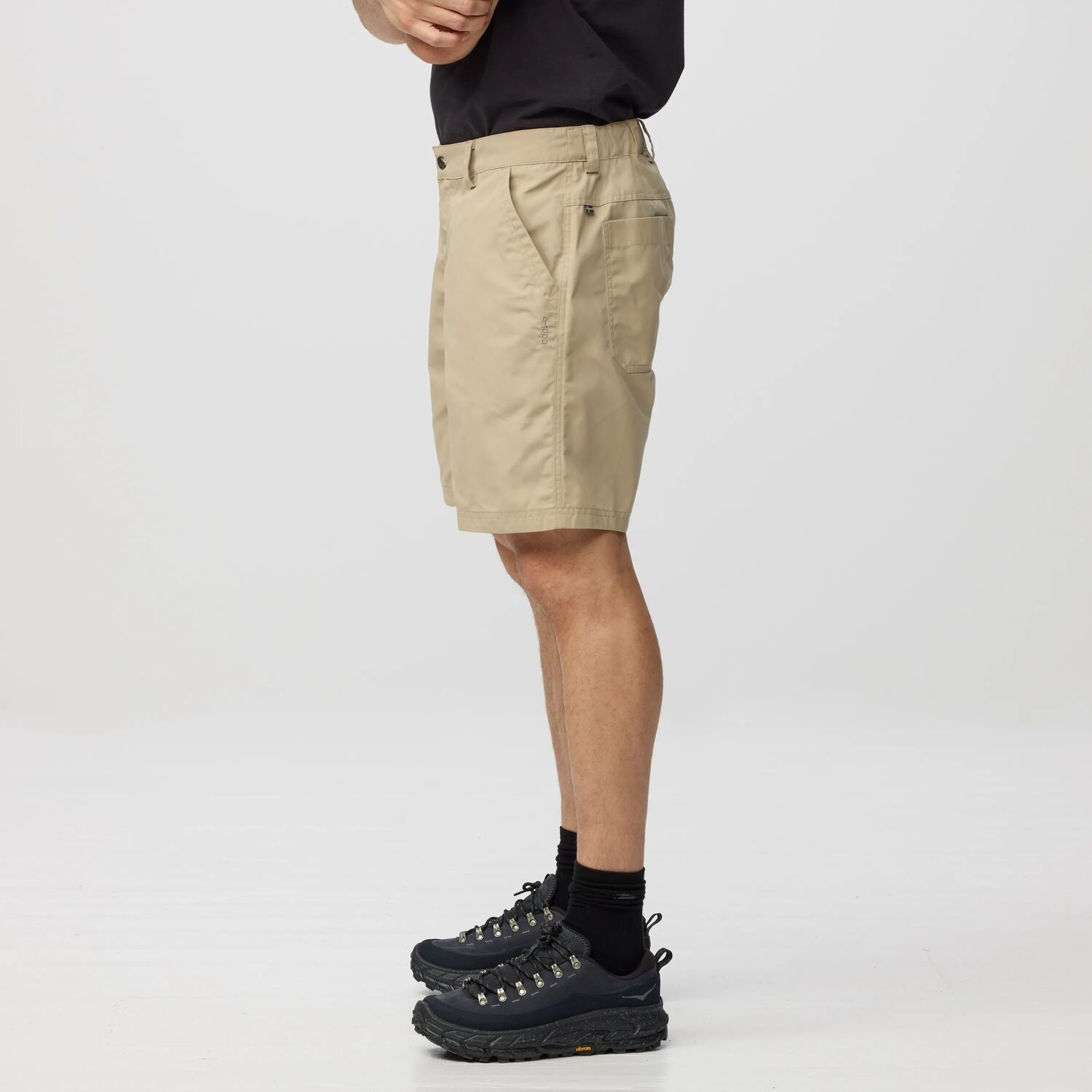 Person wearing beige shorts and black hiking boots on a white background